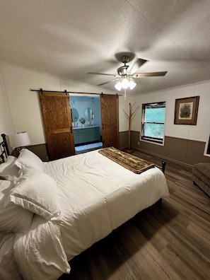 Ein Schlafzimmer mit einem Bett, einem Deckenventilator, einem Fenster mit Jalousien und einer Tür zu einem Badezimmer.