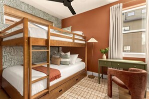 A bunk bed with a desk and chair, a window with curtains, and a patterned wall. - Eastside ATX Social Golf Sim Hot Tub Sauna (Austin)