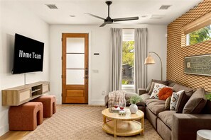 Ein Wohnzimmer mit Fernseher, Deckenventilator, Sofa, Couchtisch und einer Tür.