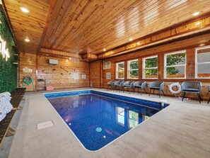 Ein Innenpool mit Holzwänden und -decke, umgeben von Stühlen und einem Tisch am Beckenrand.