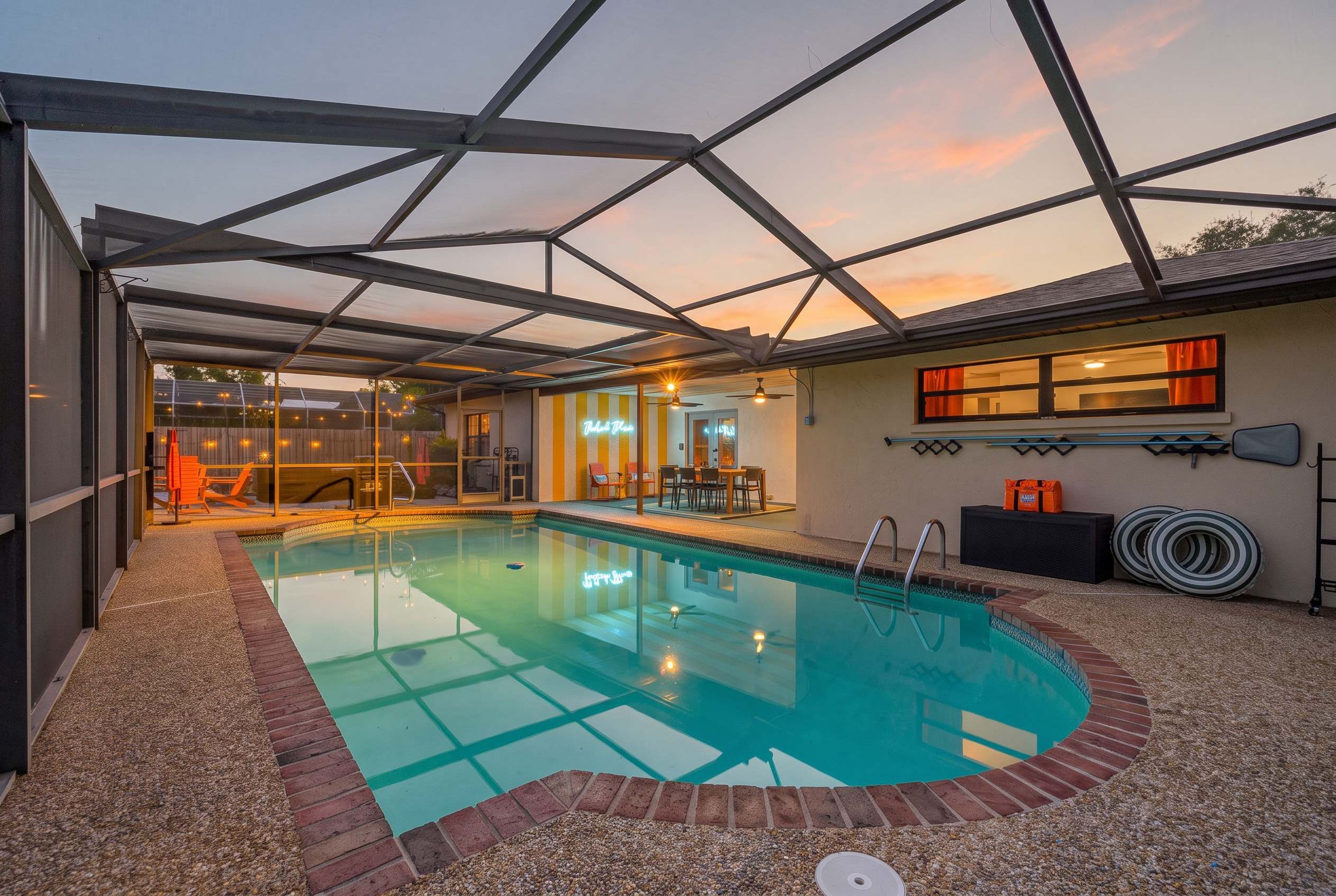 An indoor swimming pool with a glass ceiling, surrounded by a pebble-covered floor, and a seating area with a neon sign.