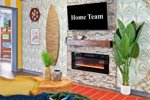 Ein Wohnzimmer mit Kamin, einer Wandmontage-Fernseher und tropischem Wandpapier.