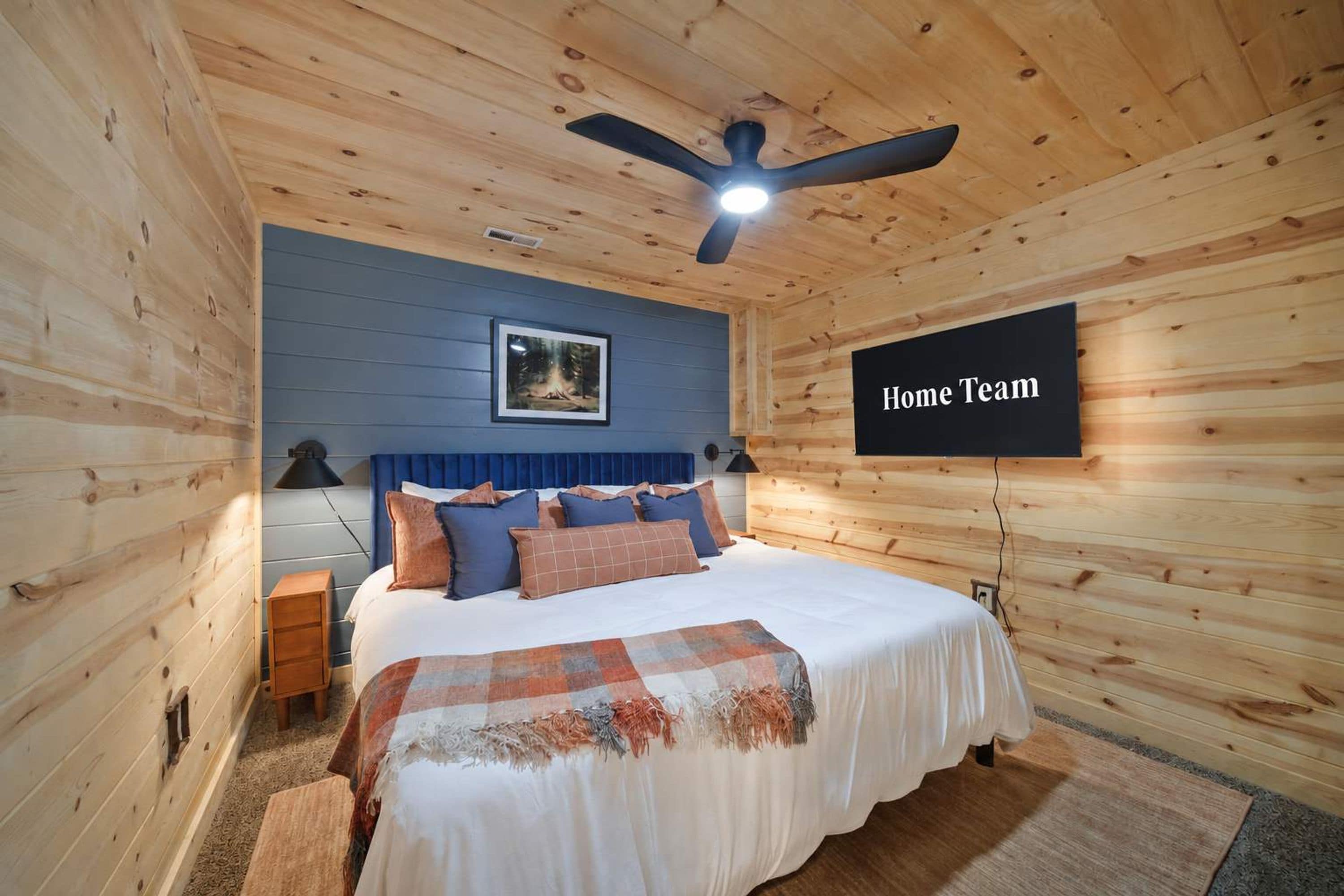 A bedroom with a bed, a ceiling fan, a framed picture, and a 'Home Team' sign.