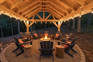 Un área de estar al aire libre con techo, sillas de madera y una chimenea en el centro.