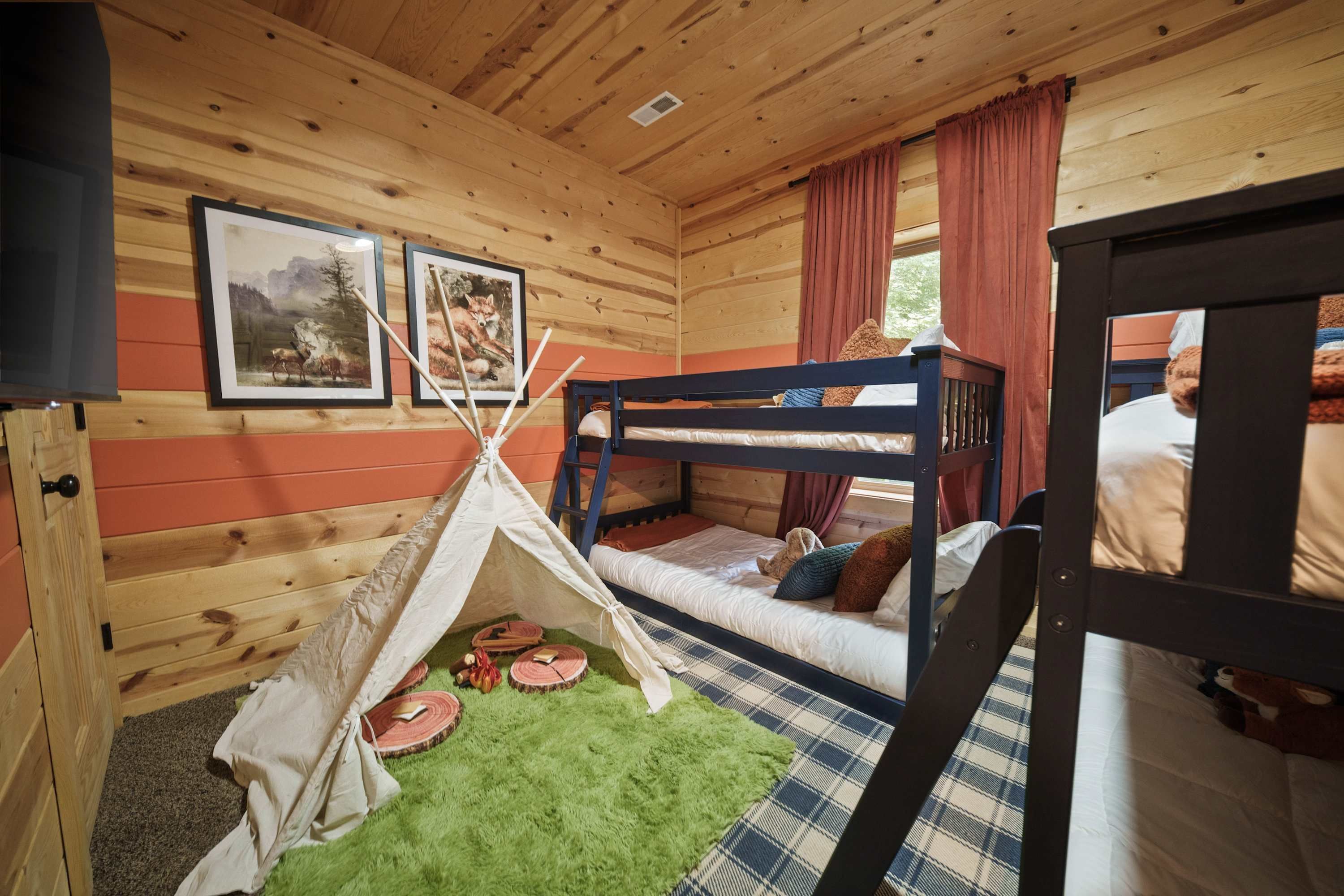 Una habitación acogedora con paredes de madera, una cama litera, un tipi y dos cuadros enmarcados.