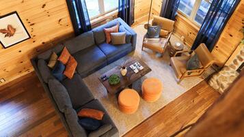 Interior acogedor de una cabaña con un sofá seccional, una mesita redonda y un sillón de cuero.