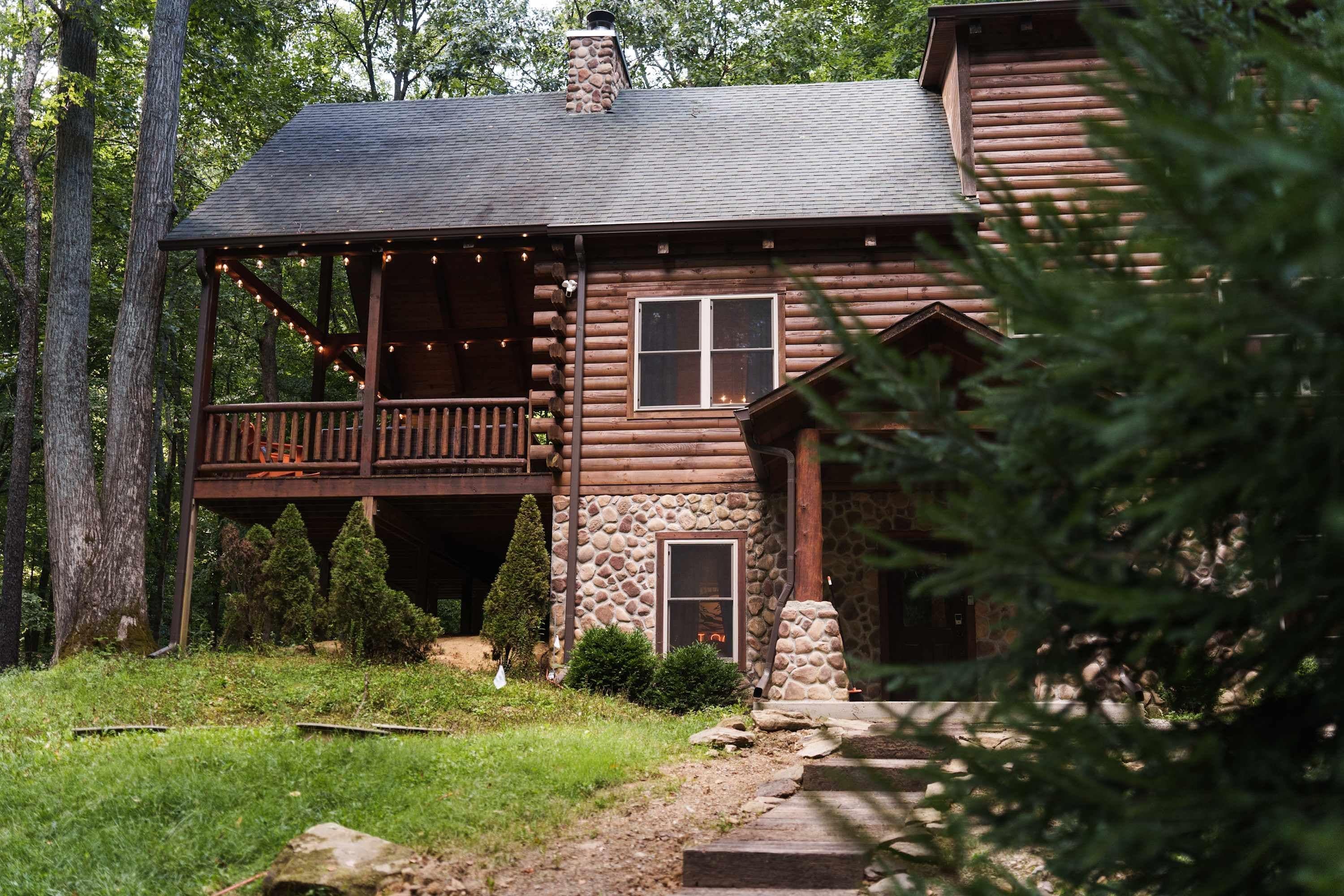 A rustic log cabin with a porch, stone foundation, and a chimney.