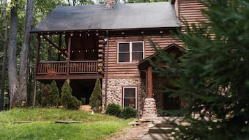A rustic log cabin with a porch, stone foundation, and a chimney.