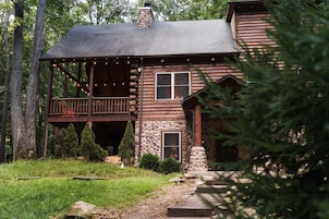 A rustic log cabin with a porch, stone foundation, and a chimney.