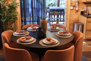 Una mesa redonda con seis sillas, cada una con una servilleta doblada y un plato. Un jarrón con ramas está sobre la mesa.