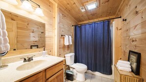 Un baño de cabaña de madera con lavamanos, inodoro y cortina de ducha.