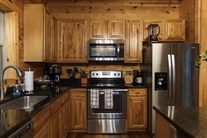 Una cocina con gabinetes de madera, electrodomésticos de acero inoxidable, incluyendo un microondas, estufa y refrigerador, además de una cafetera.