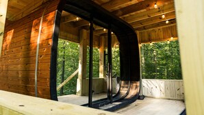 Una cabaña de madera con entrada arqueada, un muelle de madera y vistas del bosque circundante.