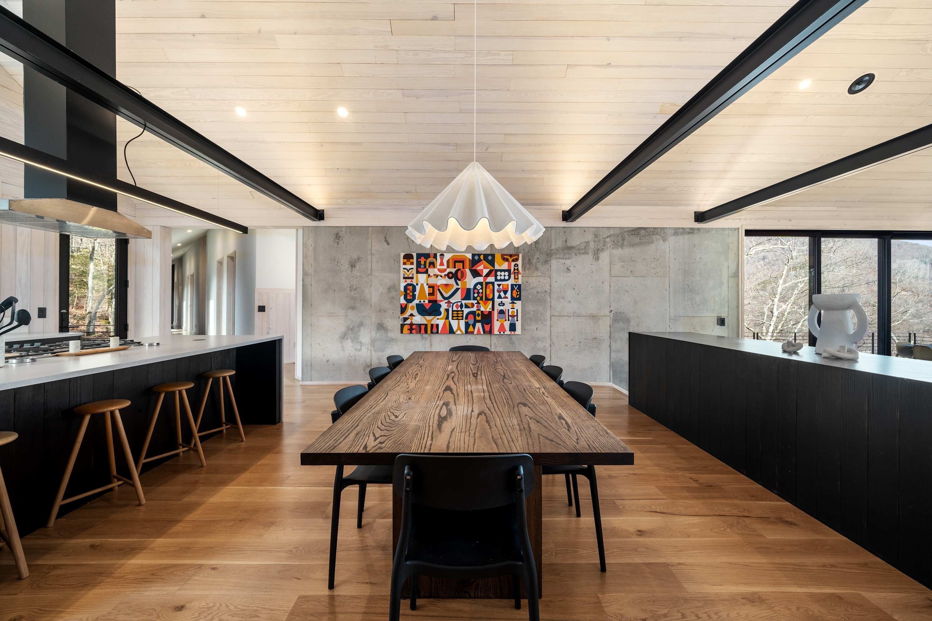Una cocina moderna con una mesa de madera y taburetes de bar, un ventanal grande y una original obra de arte en la pared.