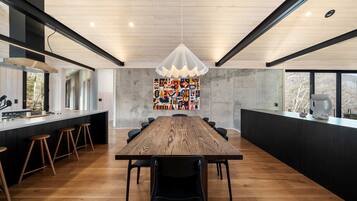 Una cocina moderna con una mesa de madera y taburetes de bar, un ventanal grande y una original obra de arte en la pared.