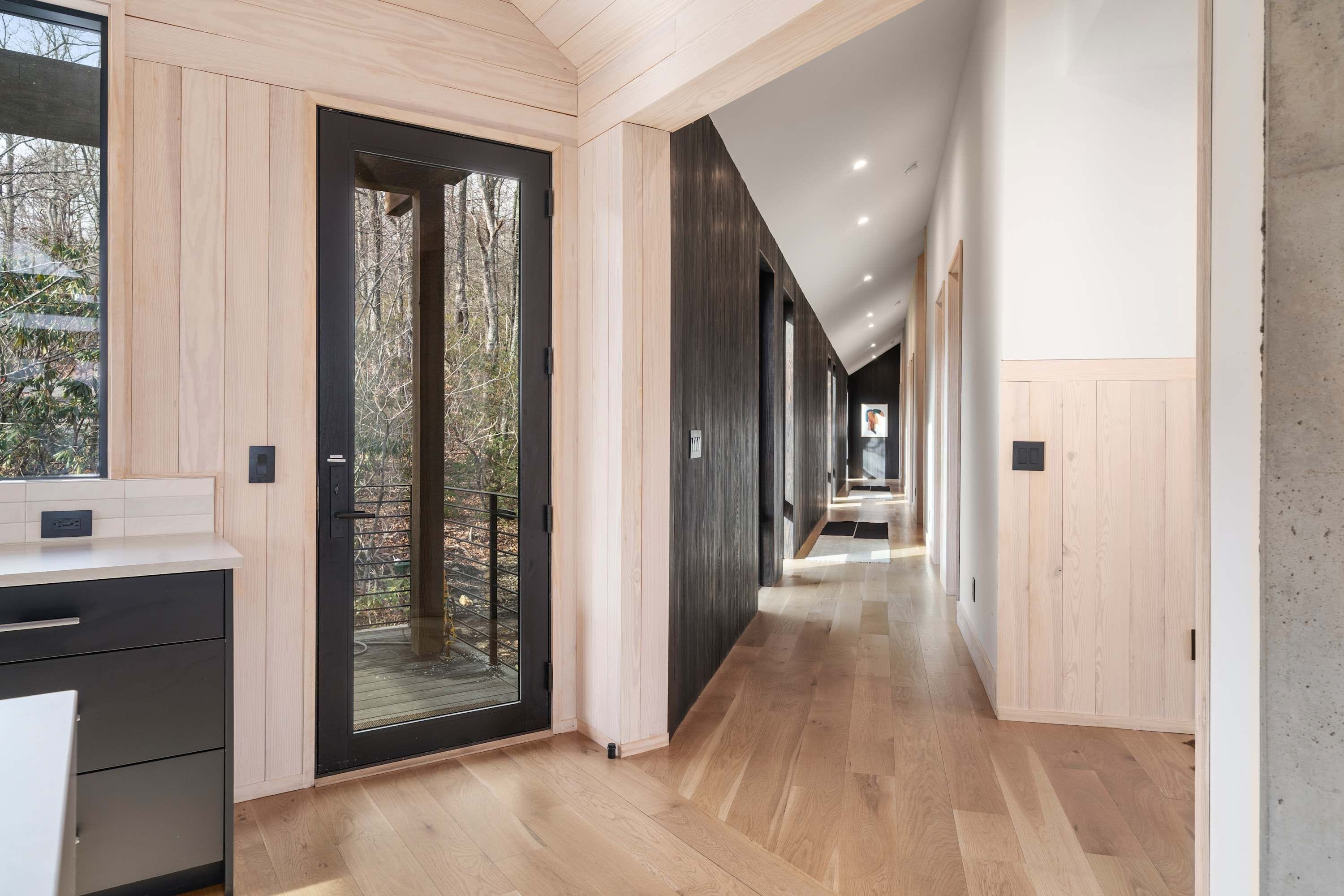 Un interior moderno con piso de madera, una zona de cocina con mostrador y vista a una terraza exterior a través de una puerta de vidrio.