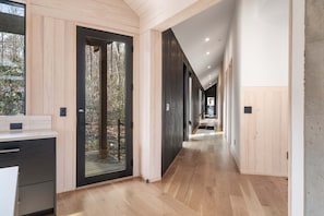 Un interior moderno con piso de madera, una zona de cocina con mostrador y vista a una terraza exterior a través de una puerta de vidrio.