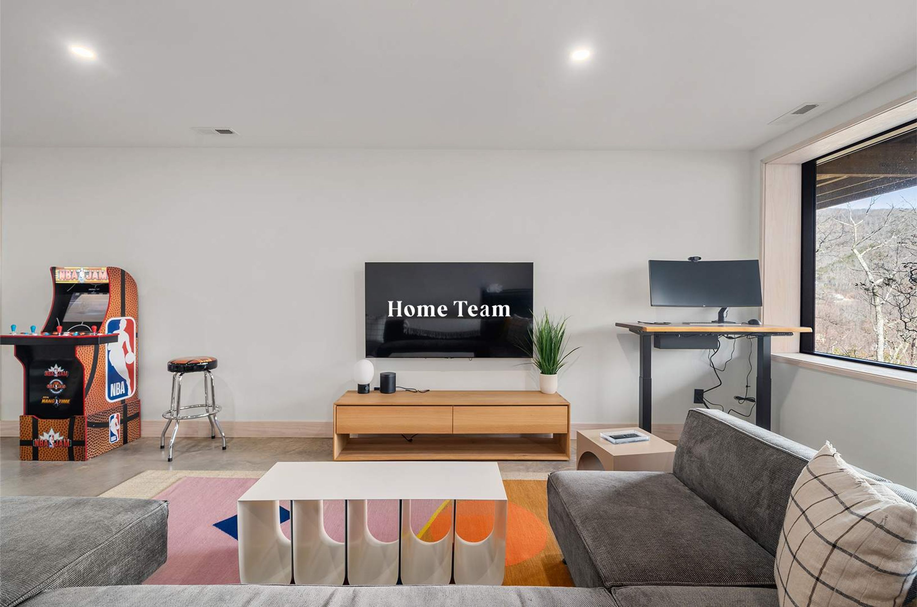 Una sala de estar moderna con un televisor de pantalla plana, una mesa de juegos, un sofá y un ventanal con vistas.