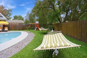 A backyard with a swimming pool, a wooden fence, a hammock, and a children's play structure. - 4BR Emerald Coast Escape Pool Hot Tub Theater (Fort Walton Beach)