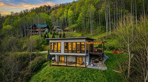 A modern two-story house with a large deck and a covered outdoor area, surrounded by dense forest. - Blissful Bluff Mtn Views Fire Pit Sleeps 6 (Candler)