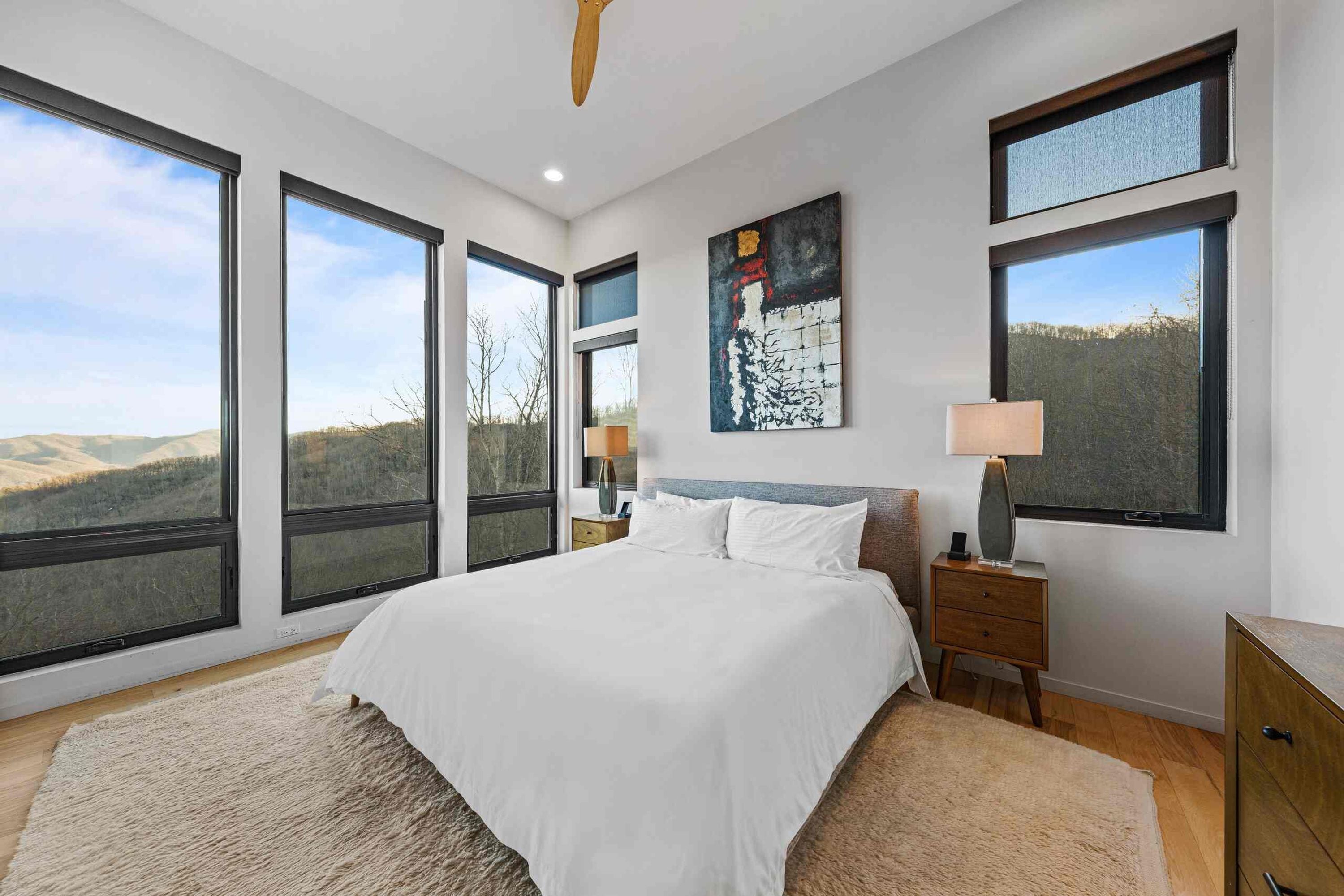 A bedroom with a large bed, two bedside tables, a nightstand, a lamp, and a painting on the wall.