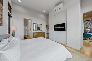 A modern bedroom with a large bed, a dresser, a mirror, and a wall-mounted TV displaying 'Home Team'. - Blissful Bluff Mtn Views Fire Pit Sleeps 6 (Candler)