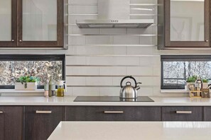 A modern kitchen with dark wooden cabinets, a stainless steel kettle, and a window with a view of trees. - Blissful Bluff Mtn Views Fire Pit Sleeps 6 (Candler)