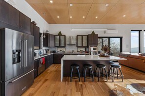 A modern kitchen with a central island, bar stools, and a large refrigerator. - Blissful Bluff Mtn Views Fire Pit Sleeps 6 (Candler)