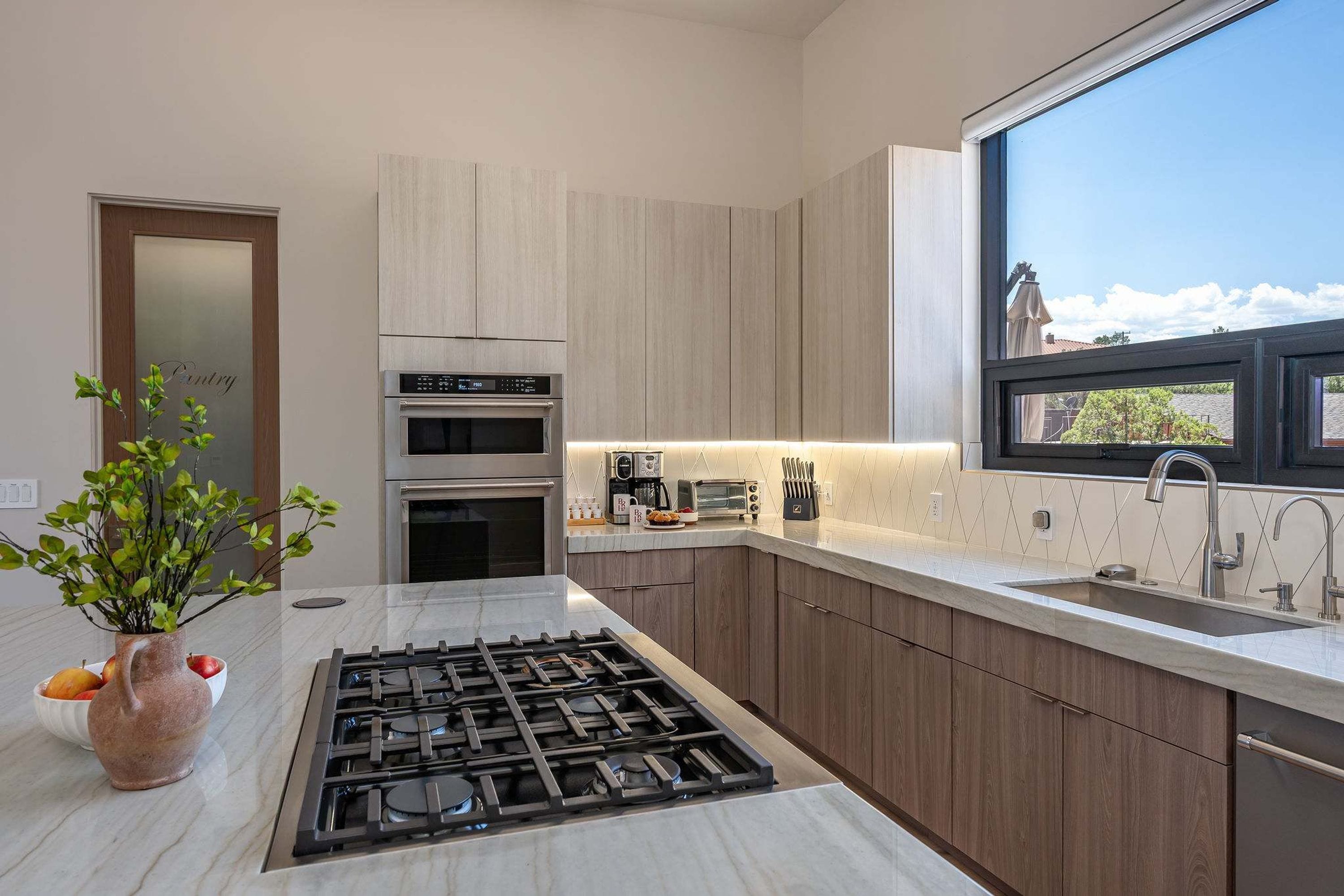 Una cocina moderna con estufa a gas, horno integrado y ventana con vistas a una zona residencial.