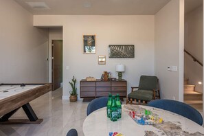Ein Wohnzimmer mit Billardtisch, einer Couch, einem Sessel, einem Couchtisch und einer Vitrine mit Dekoration.