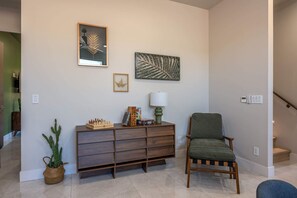 Ein Wohnzimmer mit einem Holzschrank, einem grünen Sessel und zwei gerahmten Kunstwerken an der Wand.
