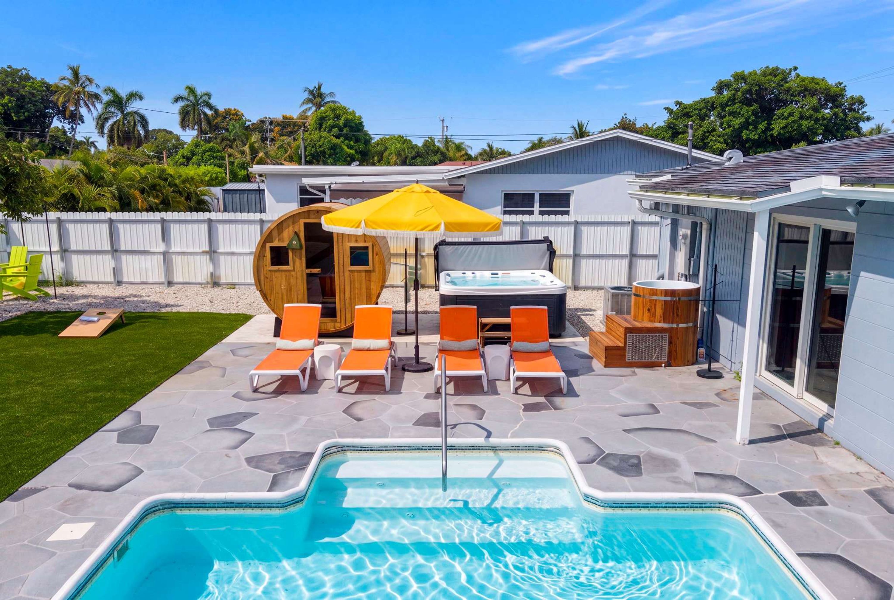 A backyard with a swimming pool, lounge chairs, a hot tub, and a wooden sauna.