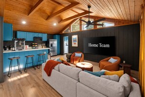 Ein modernes Wohnzimmer mit großem Fernseher, einer Couch und einer Küchenzeile mit blauen Schränken.
