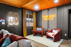 A room with a wooden ceiling, a large window with curtains, a neon sign, two red chairs, and a bed with multiple pillows. - Heatwave Hideaway Pool Pickleball Games (Tempe)