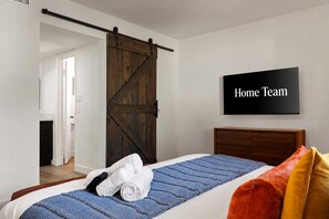 Ein Schlafzimmer mit Bett, einer Schiebetür im Bauernhausstil, einem an der Wand montierten Fernseher und einem Flur.