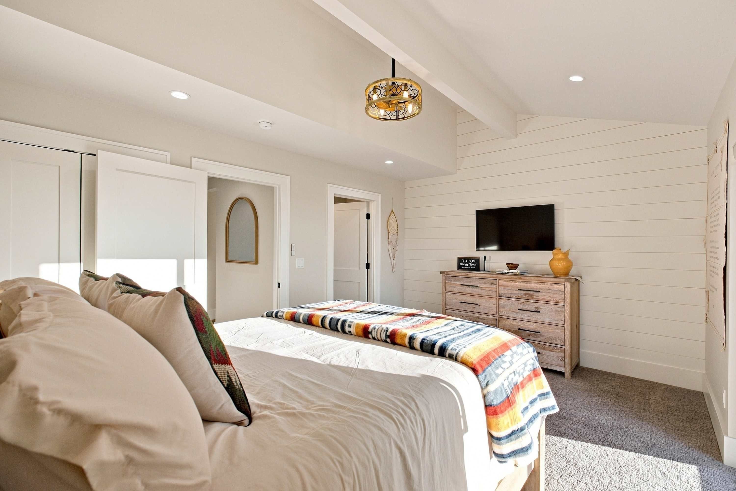 A bedroom with a bed, a dresser, a television, and a ceiling light fixture.