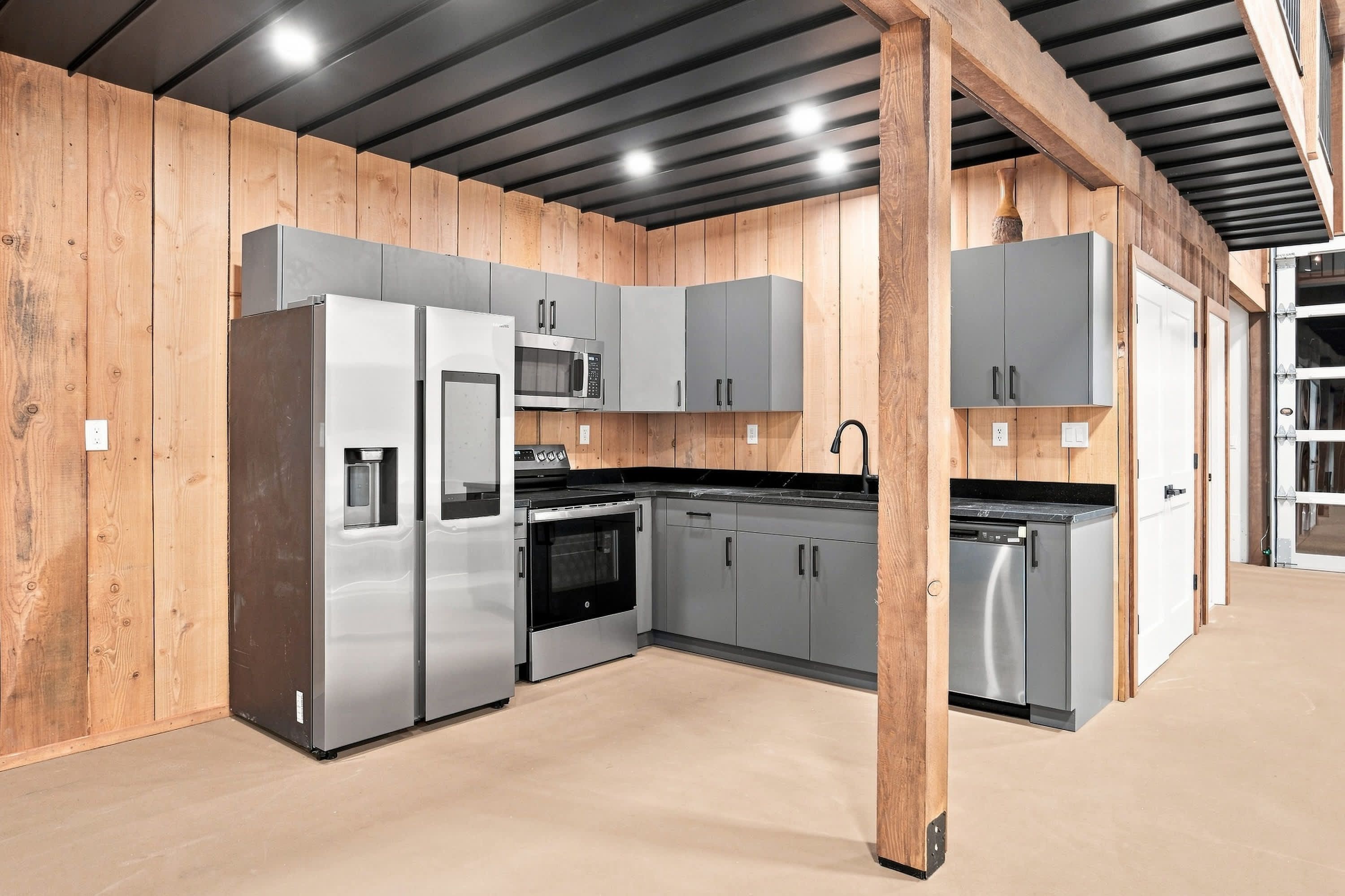 A modern kitchen with stainless steel appliances, wooden panel walls, and a concrete floor.