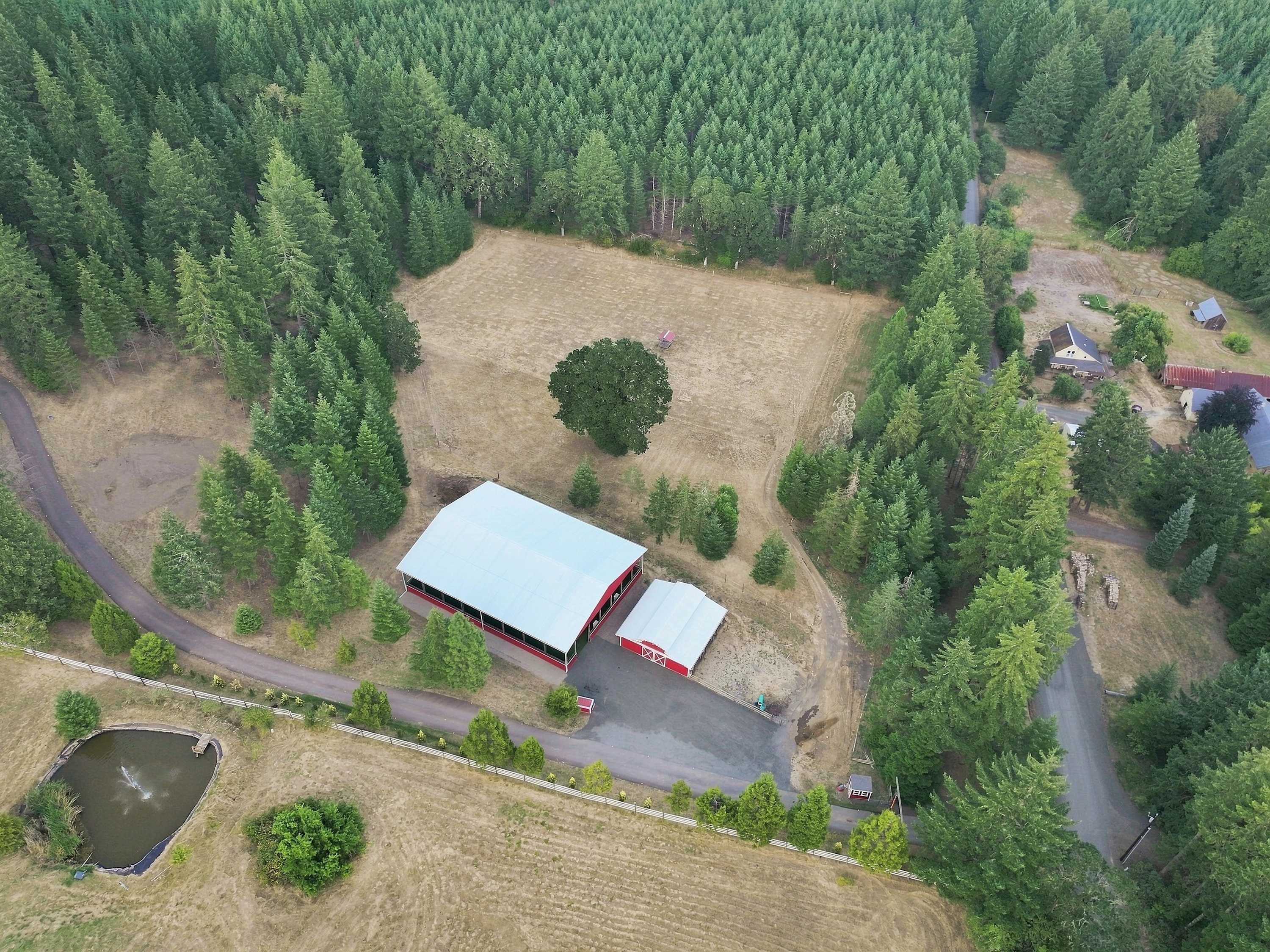 An aerial view of a property with a large building, a fenced area, and a road.