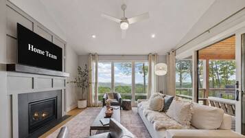 A modern living room with a fireplace, a flat-screen TV, a sofa, and a view of the outdoors.