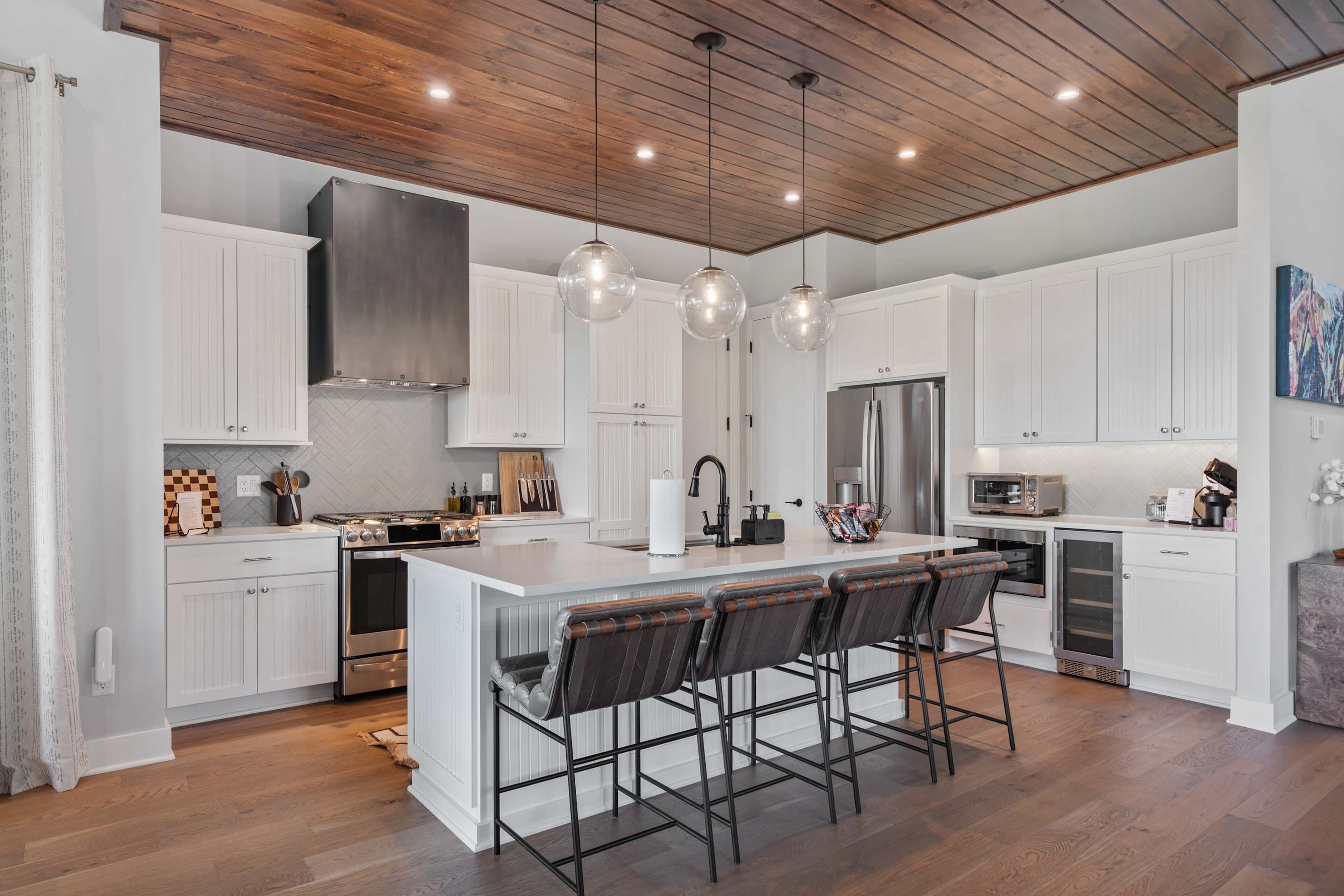 A modern kitchen with white cabinetry, a central island with bar stools, stainless steel appliances, and pendant lighting.