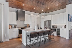 A modern kitchen with white cabinetry, a central island with bar stools, stainless steel appliances, and pendant lighting.