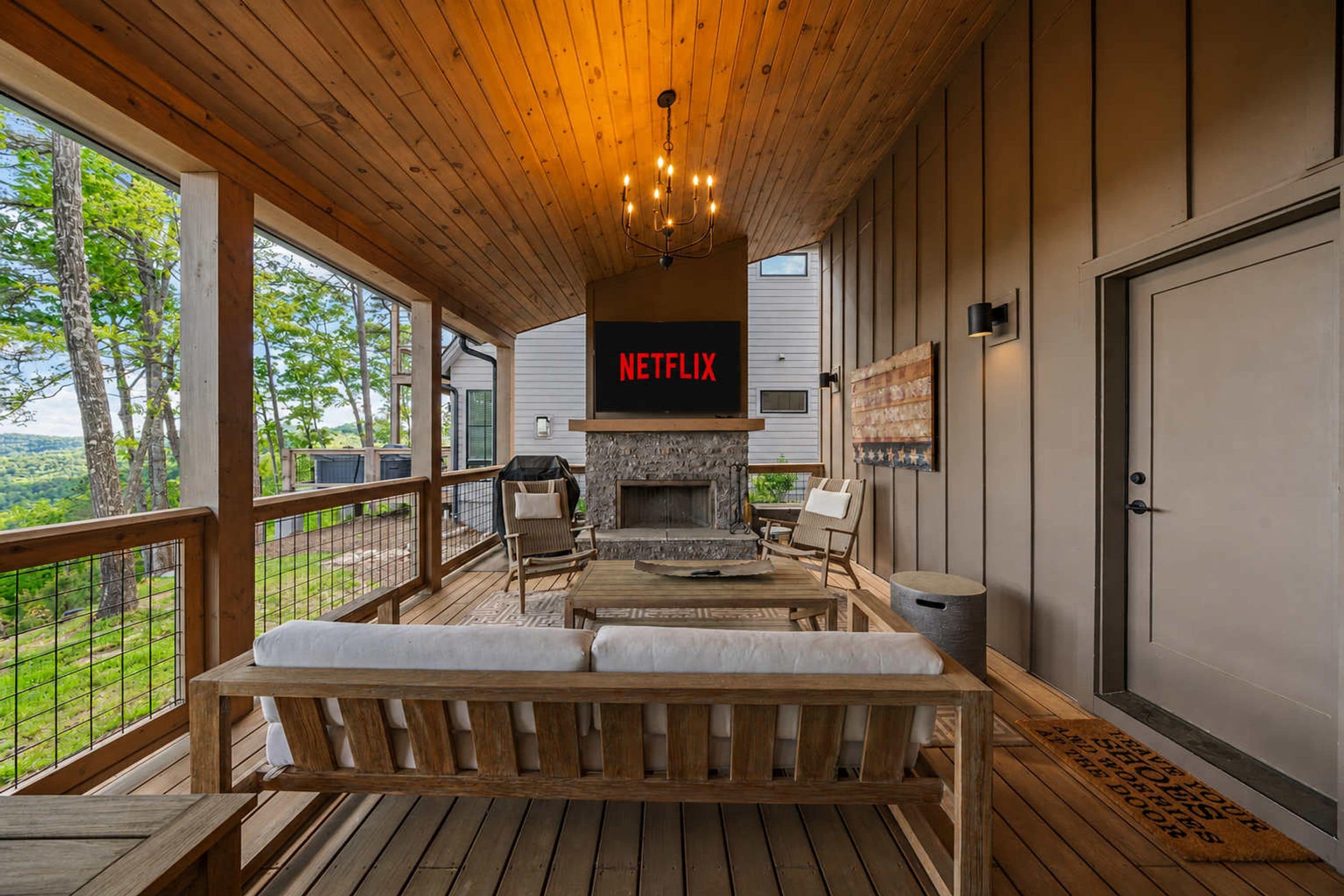 A wooden deck with a stone fireplace, outdoor seating, and a Netflix TV mounted on the wall.