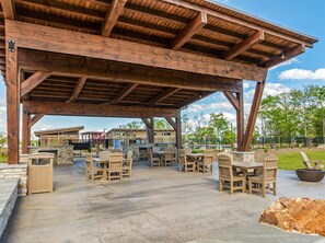 An outdoor patio with wooden tables and chairs, a stone fireplace, and a view of a residential area. - High Country Club Modern Mountain Escape (Deep Gap)