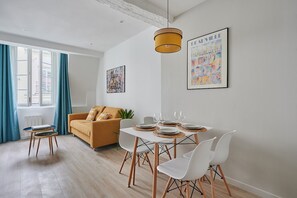 A modern living room with a dining area, featuring a sofa, a table set for four, and artwork on the walls. - Sublime  appartment  in center of Paris (Paris)