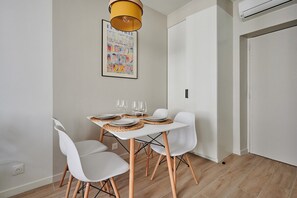 Un coin repas avec une table blanche dressée pour quatre personnes, des chaises blanches, une suspension jaune et un tableau encadré accroché au mur.