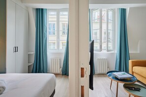 Une chambre d’hôtel avec un lit, un canapé, une télévision et une fenêtre avec des rideaux.