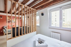Ein Schlafzimmer mit Bett, Fenster, Heizkörper und einer Holzwand.