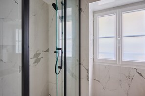 A glass-enclosed shower with a handheld showerhead, a window with a view, and marble walls. - Charming Studio Center of Paris-Montorgueil (Paris)