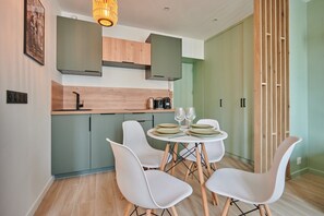 A modern kitchen with a dining area, featuring a round table with chairs, a coffee machine, and a hanging light fixture. - Charming Studio Center of Paris-Montorgueil (Paris)