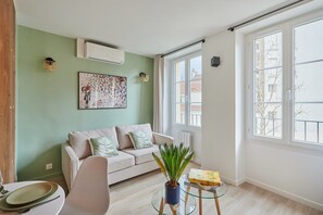 A living room with a sofa, a coffee table with a plant, and a window with a view of buildings. - Charming Studio Center of Paris-Montorgueil (Paris)